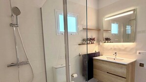 A modern bathroom with a glass shower enclosure, a toilet, a sink with a mirror above, and a small window. - Detached house in the center of Santa Cruz de Tenerife (Santa Cruz)