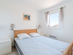 A bedroom with a bed, two bedside tables, a wall-mounted lamp, a window with curtains, and a small painting on the wall. - Comfortable House with Pool, Terrace, and Parking in Saint-Pierre-La-Mer (Fleury-Saint-Pierre-la-Mer)