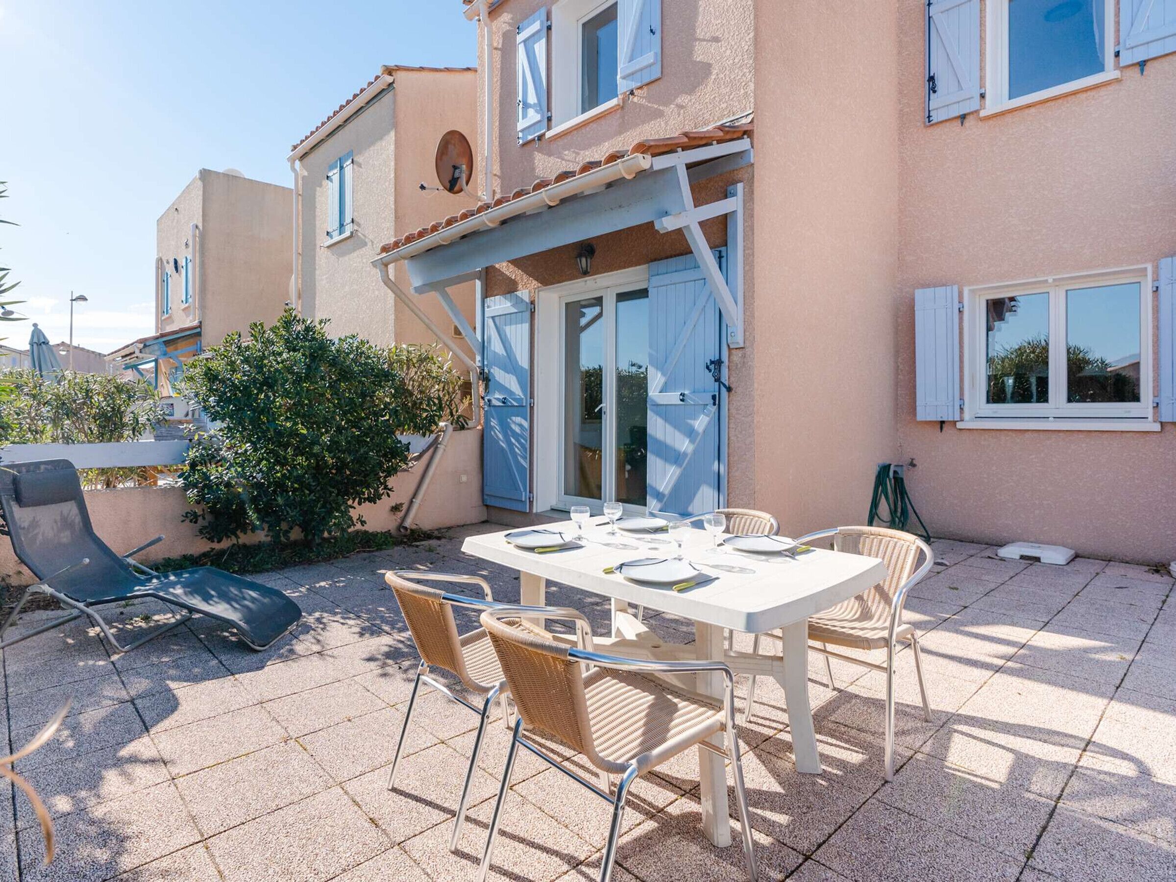 A patio with a table set for four, surrounded by wicker chairs, and a lounge chair.