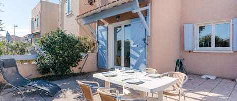 A patio with a table set for four, surrounded by wicker chairs, and a lounge chair.