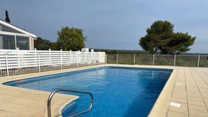 A rectangular swimming pool with a metal ladder, surrounded by a white fence and beige tiles. - Comfortable House with Pool, Terrace, and Parking in Saint-Pierre-La-Mer (Fleury-Saint-Pierre-la-Mer)