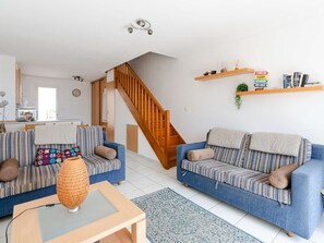 Ein Wohnzimmer mit zwei Sofas, einem Couchtisch, einer Holztreppe und einer Küche im Hintergrund.