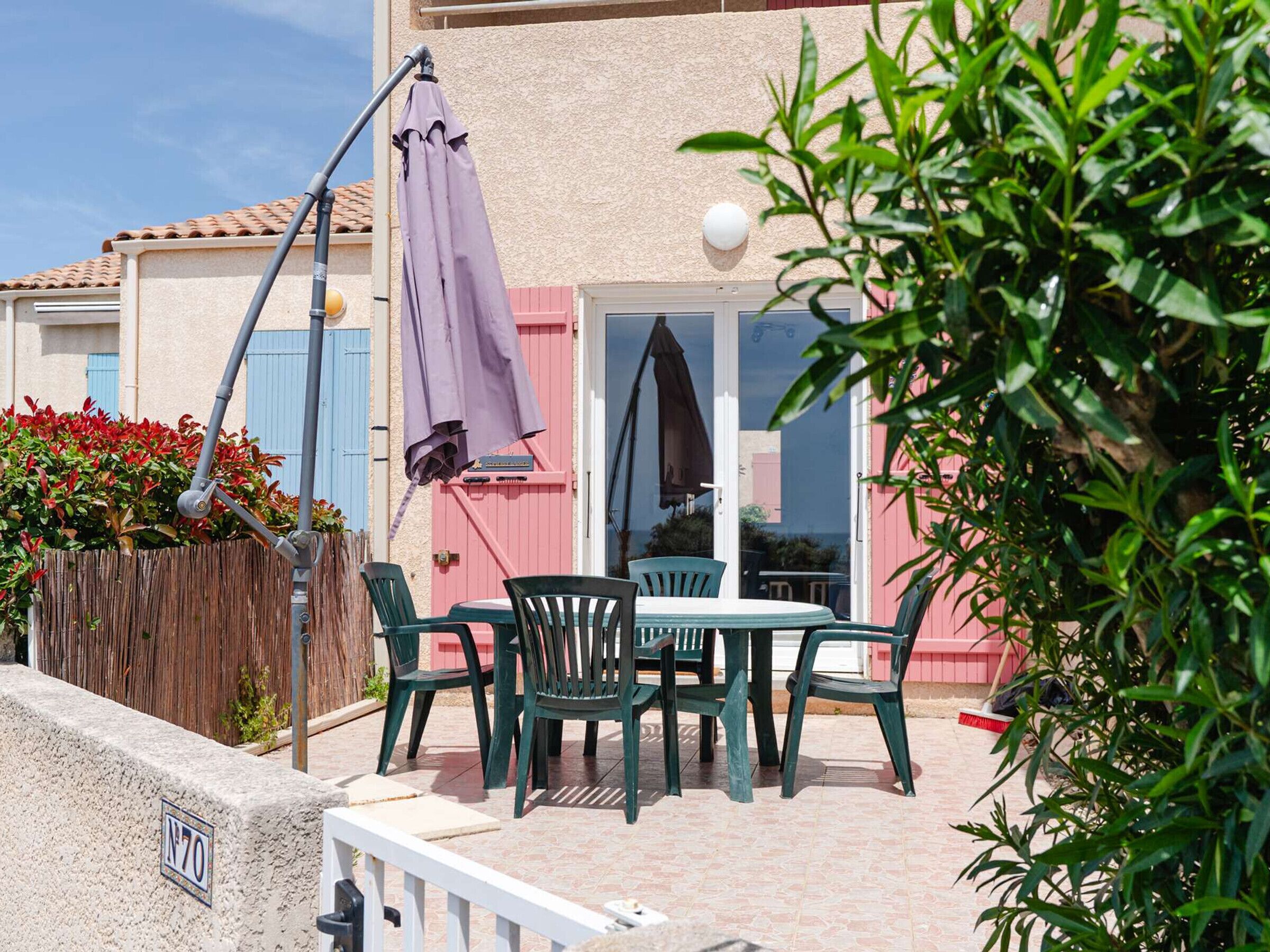 Une terrasse extérieure avec une table et des chaises, une clôture en bois et un bâtiment doté d’une porte rose.