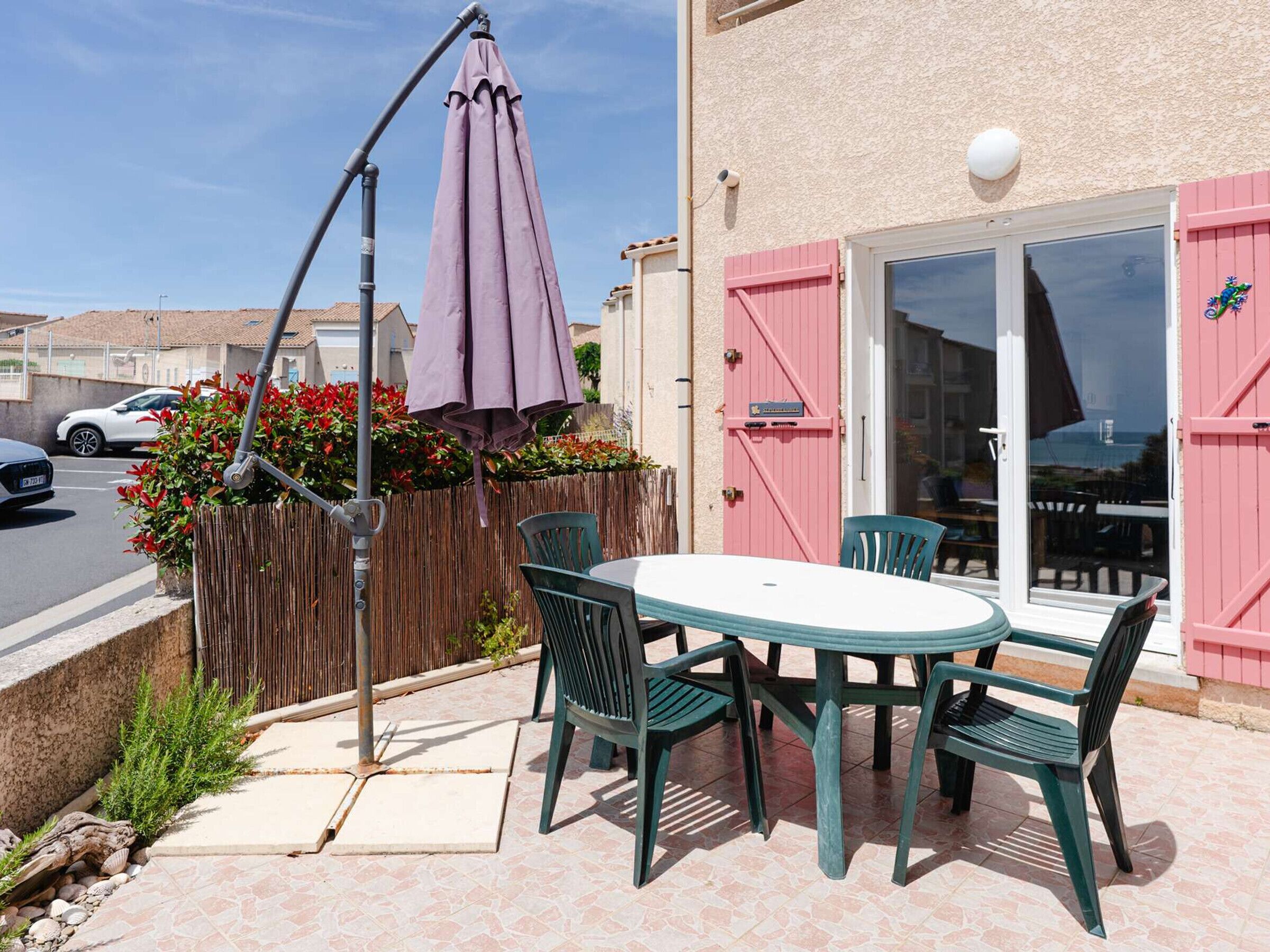 Une terrasse extérieure avec une table et des chaises, un parasol violet et une clôture en bois ornée de fleurs.