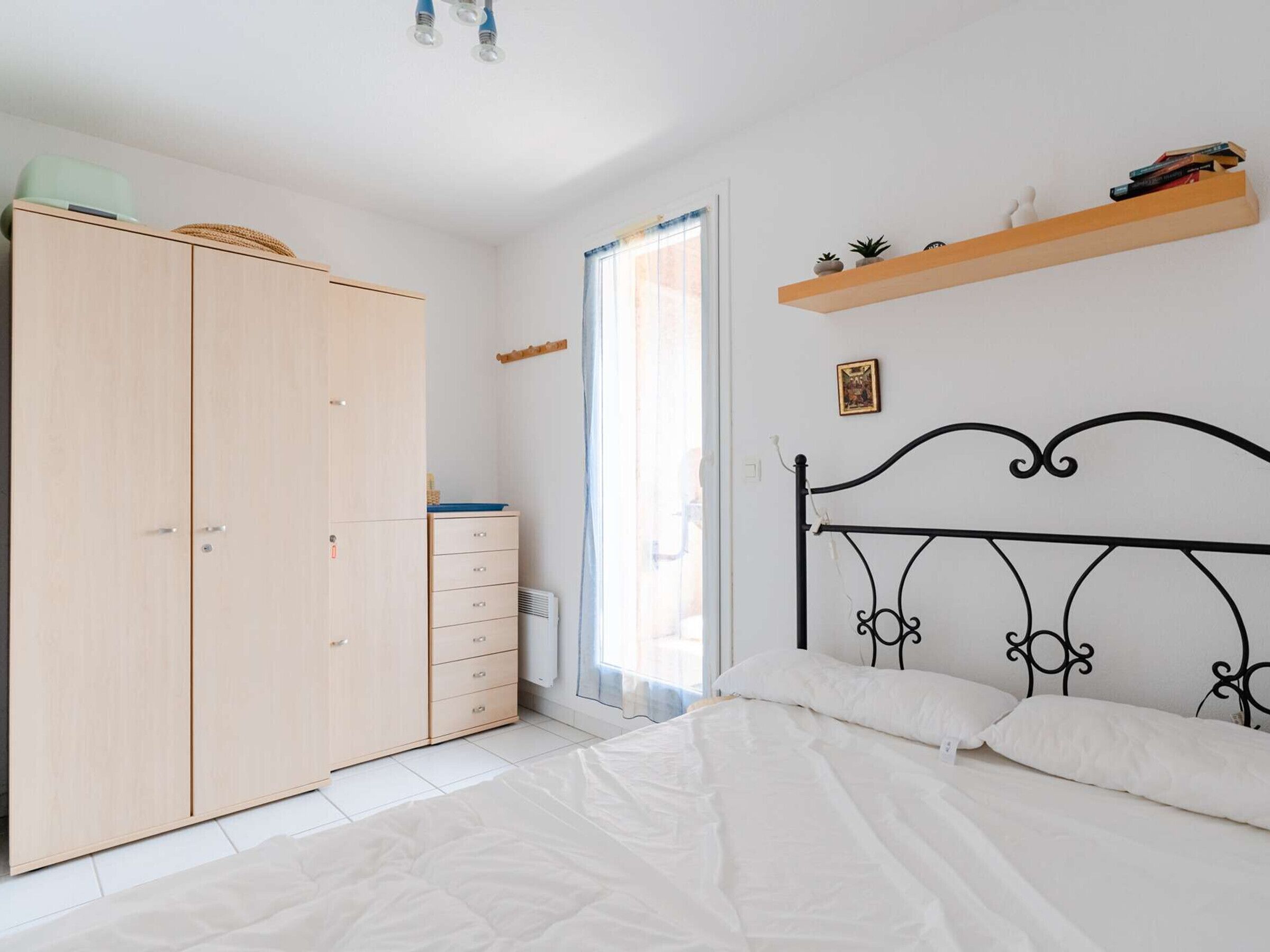 Een slaapkamer met een bed, een kledingkast, een plank en een raam.