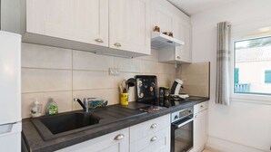 A modern kitchen with white cabinets, a black countertop, a built-in oven, and a window with curtains. - Air-conditioned apartment with pool - 4 guests (Narbonne)
