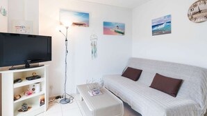 A modern living room with a flat-screen TV, a floor lamp, a sofa, and wall art. - Air-conditioned apartment with pool - 4 guests (Narbonne)