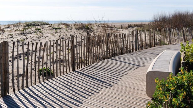 A wooden boardwalk leading to a beach with a sandy landscape and sparse vegetation.