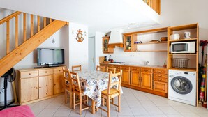 A compact kitchen with wooden cabinets, a dining table, chairs, a washing machine, and a TV.