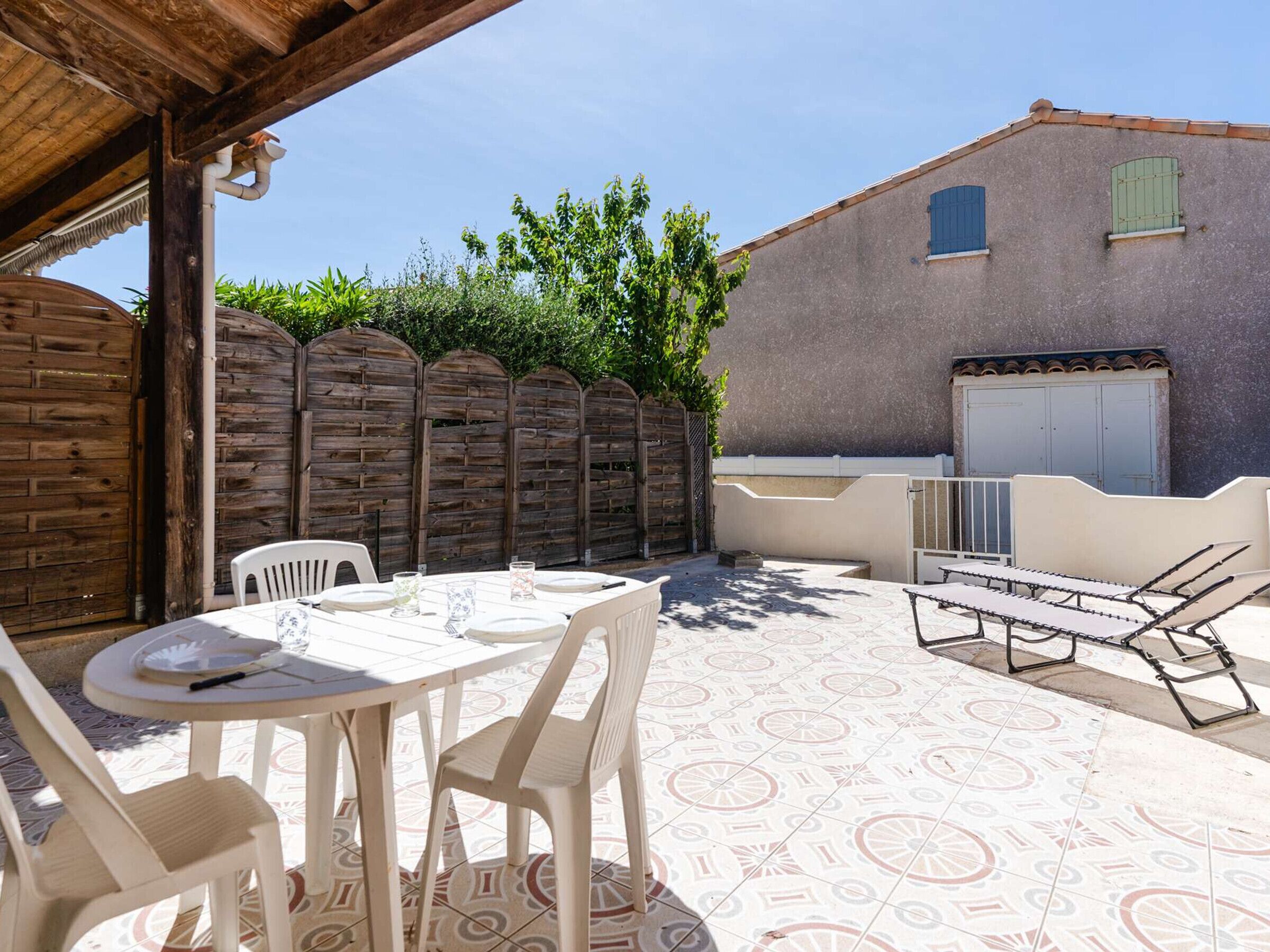An outdoor patio with a table and chairs, a barbecue area, and a tiled floor.