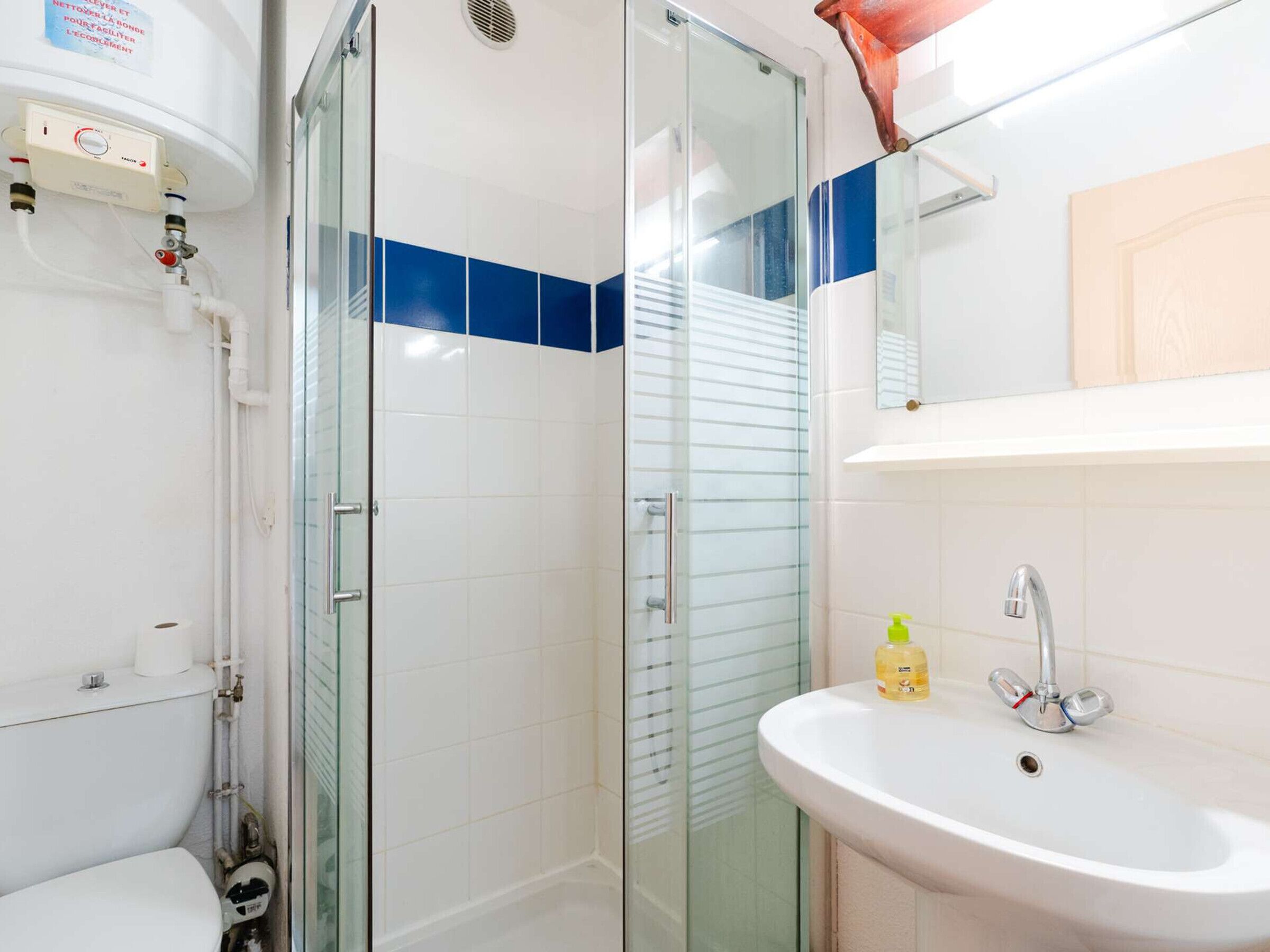 A bathroom with a glass shower enclosure, a white sink with a mirror above it, and a toilet visible to the left.