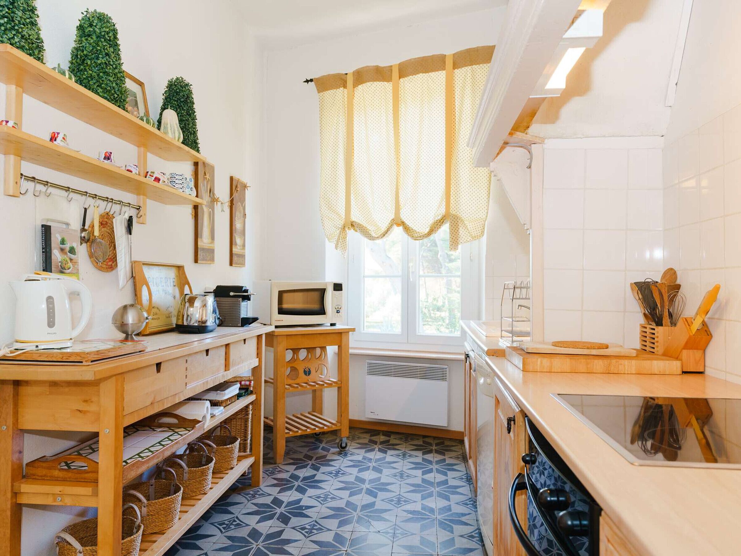Una cocina con estantes de madera, microondas, hervidor y ventana con cortinas.