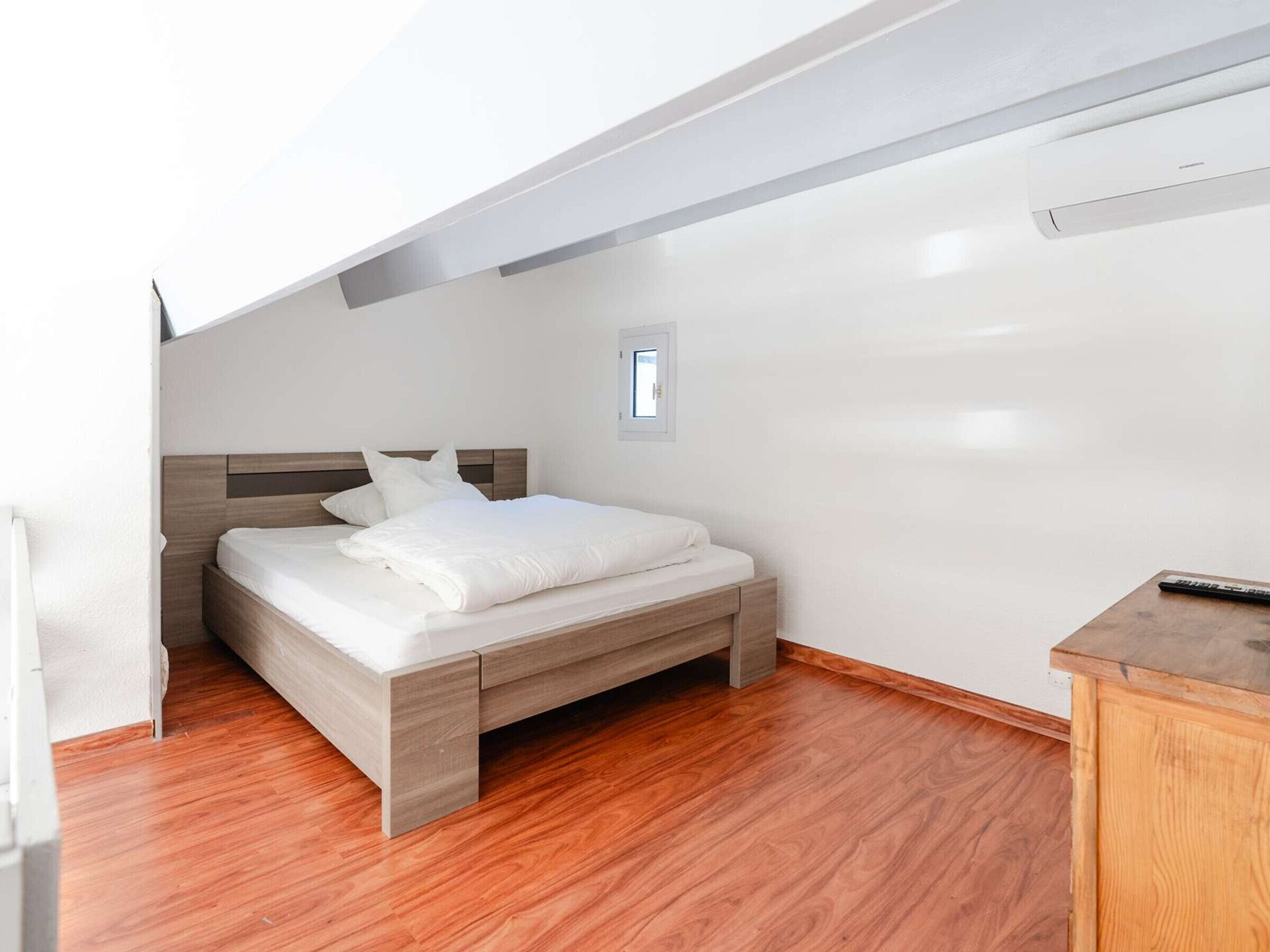 A modern bedroom with a wooden bed, a small desk, and a window.