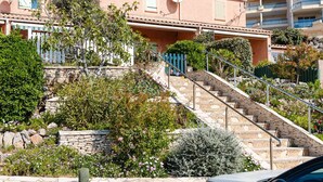 A residential building with a stone staircase leading to a balcony, surrounded by lush greenery and a stone wall.