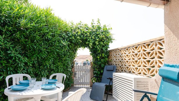 Un patio con una mesa redonda, sillas de plástico blancas y una silla reclinable azul.