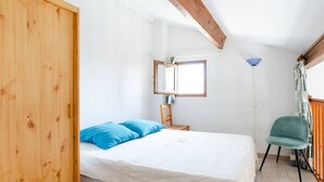 Un dormitorio con cama, armario de madera, silla, mesita y ventana con luz natural.