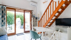 Una habitación con techo blanco, escalera de madera, televisor de pantalla plana, mesa blanca y una silla azul.