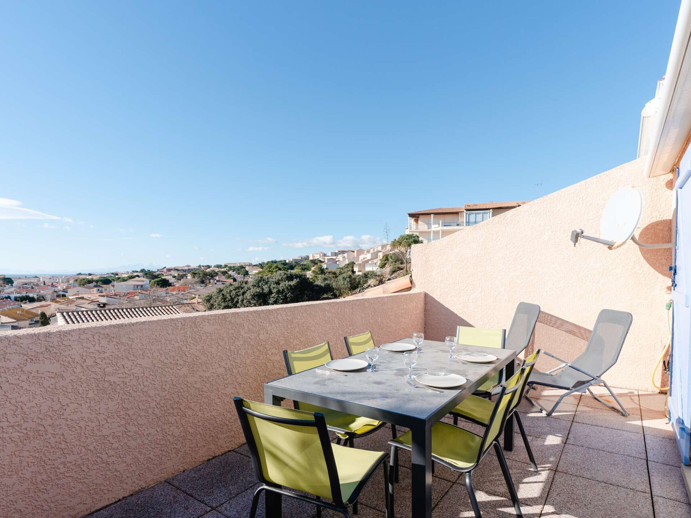 Eine Terrasse mit Tisch für vier Personen, umgeben von Stühlen, mit Blick auf eine Wohngegend.