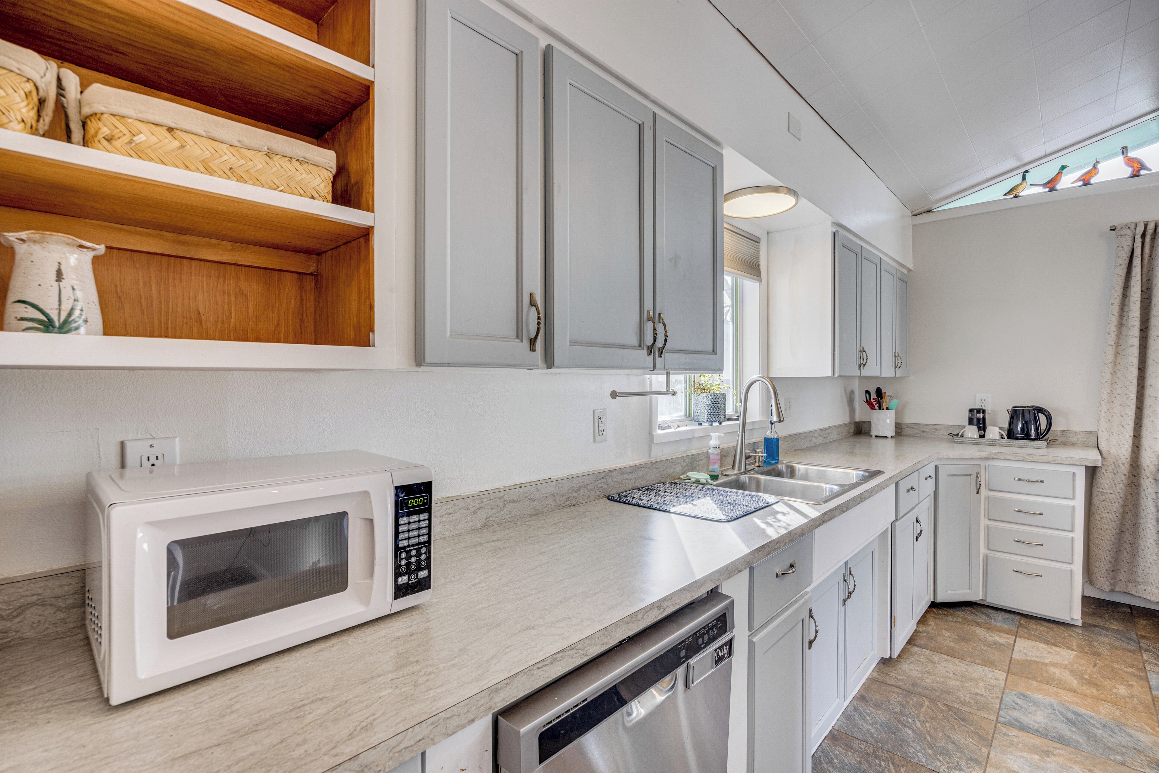 Una cocina moderna con armarios blancos, un microondas, un lavavajillas y una ventana con cortinas.