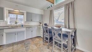 A kitchen with white cabinets, a stone tile floor, and a dining area with two chairs and a table. - 4 Mi to Riverwalk & CSU Pueblo! Home w/ Sunroom (Pueblo)