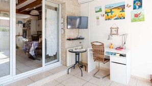 Ein gemütliches Zimmer mit einer Schiebetür zu einem Balkon, einem an der Wand befestigten Flachbildfernseher, einem kleinen Schreibtisch mit Stuhl und verschiedenen Wandbildern.