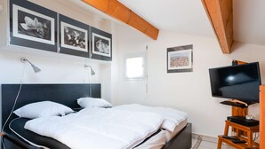 Ein Schlafzimmer mit einem Bett, einem Fernseher und gerahmten Bildern an der Wand.