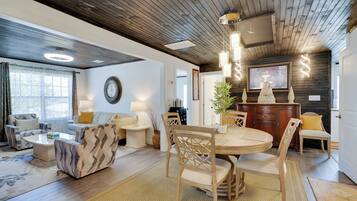 Uma sala de estar moderna com teto de madeira, uma área de jantar com mesa redonda e cadeiras, e um espaço de estar aconchegante com sofás e mesa de centro.