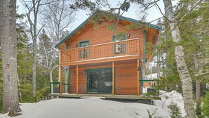 A two-story wooden cabin with a balcony, surrounded by trees and snow. - Riverfront! All-season Base 11 Mi to Sugarloaf Mtn (Kingfield)