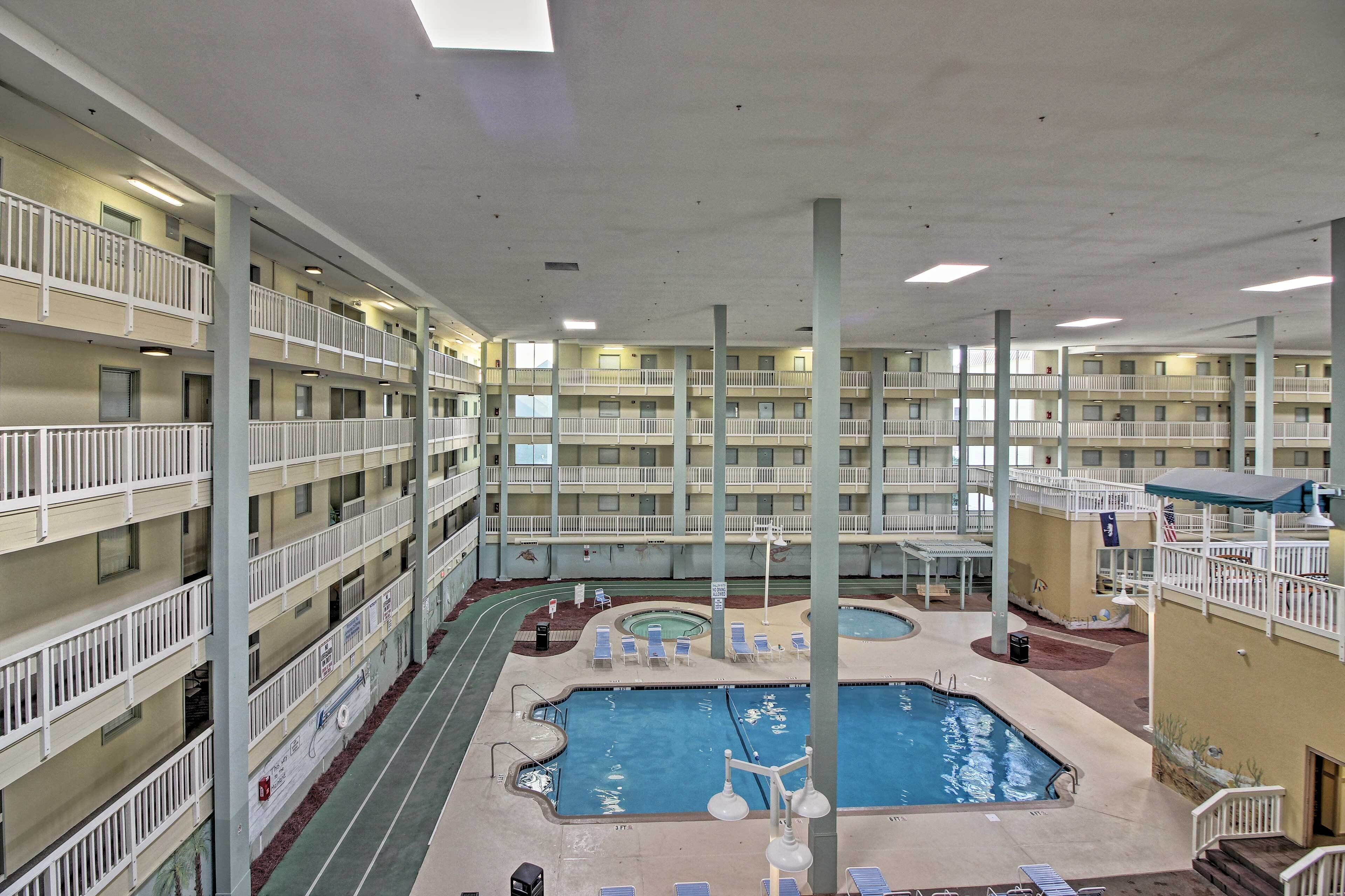 Un hotel de varios pisos con una piscina central cubierta, balcones y un área de estar techada.