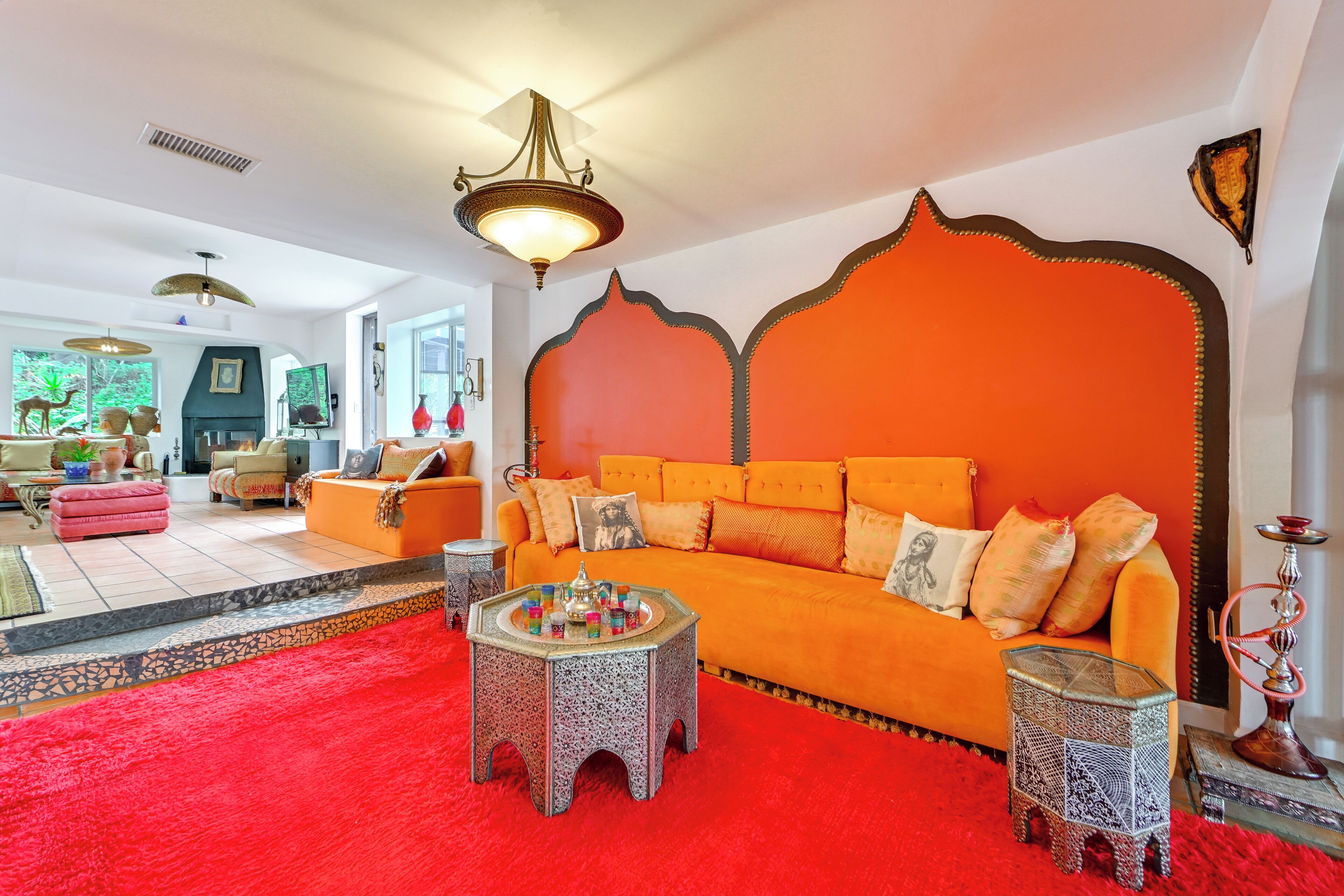 Ein Wohnzimmer mit einem orangefarbenen Sofa, einem gemusterten Hocker und einem roten Teppich.