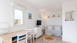Habitación pequeña y bien iluminada, con cama, escritorio y silla, televisión y una mesita.