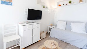 Un dormitorio moderno y minimalista con cama, televisor, armario blanco, mesita de noche pequeña y una mesa redonda de madera.
