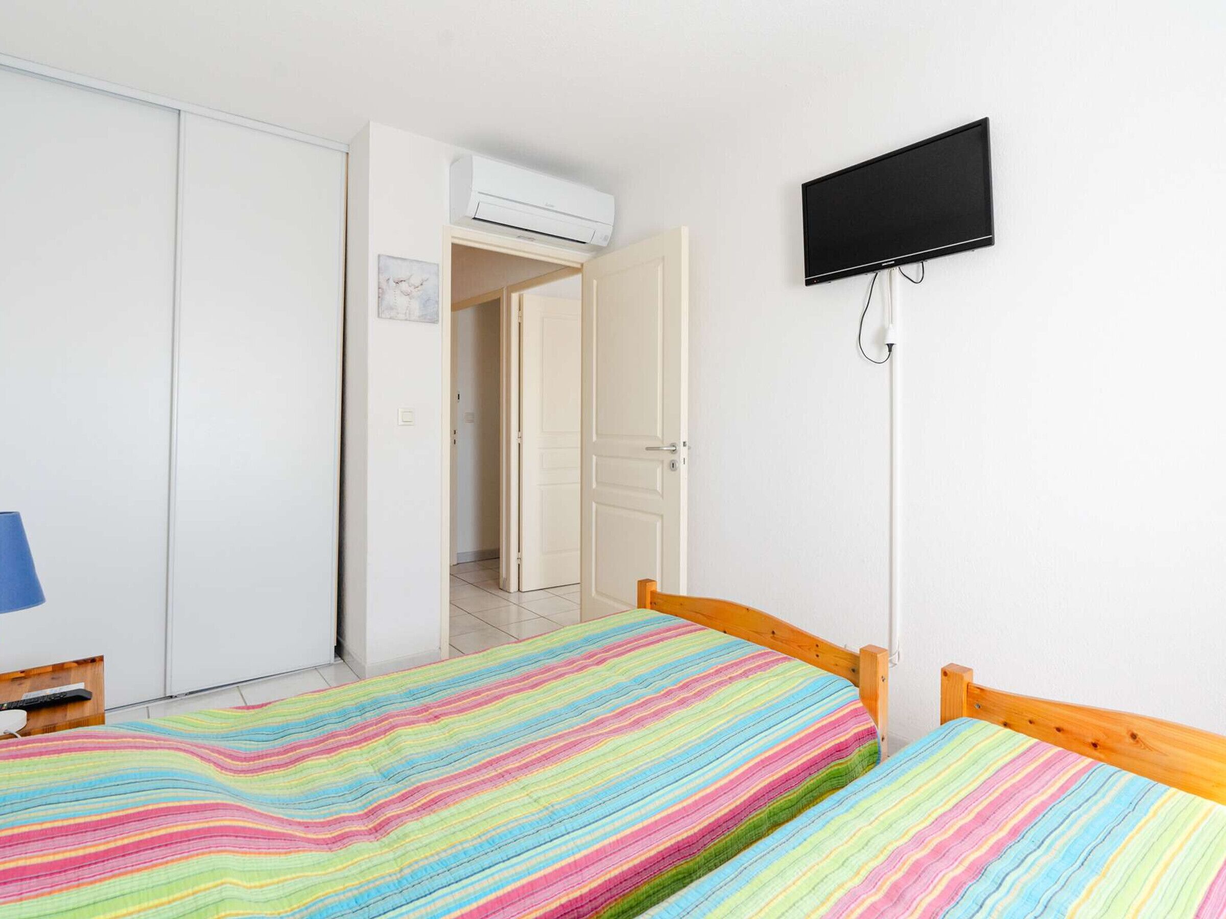 A bedroom with two beds, a TV, an air conditioning unit, and a door leading to another room.