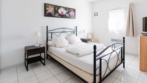 Un dormitorio ordenado con cama, mesitas de noche, televisor y ventana con cortinas.