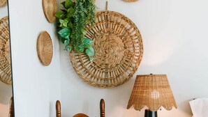 Une chaise en bois avec un coussin, une petite table d’appoint ronde en bois avec une lampe, et des paniers tressés accrochés au mur.