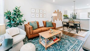 Un salon avec un canapé marron, un fauteuil blanc, une table basse en bois et une grande plante verte.