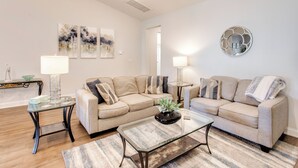 A living room with two sofas, a glass coffee table, and a lamp. There are abstract paintings on the wall and a decorative mirror. - Ultimate Golf Resort Getaway in Myrtle Beach! (Myrtle Beach)