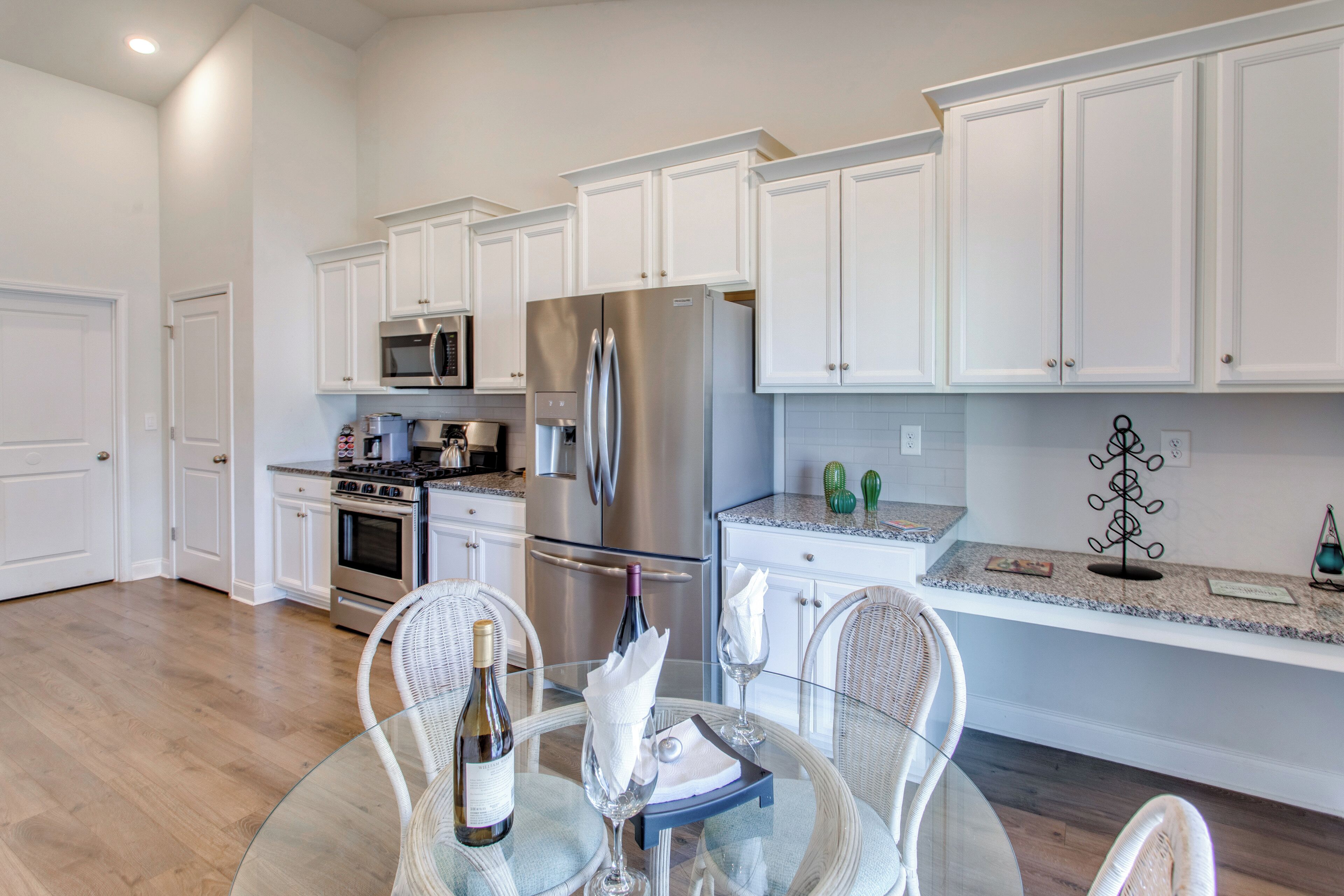 A modern kitchen with white cabinets, stainless steel appliances, and a dining area with wicker chairs and a glass table.