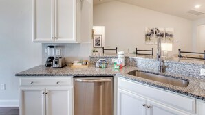 A kitchen with white cabinets, a stainless steel dishwasher, a granite countertop, and a double sink. - Ultimate Golf Resort Getaway in Myrtle Beach! (Myrtle Beach)