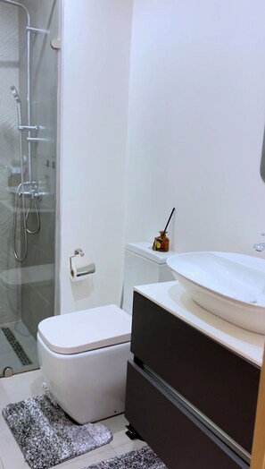 A modern bathroom with a glass shower enclosure, a toilet, a sink, and a small cabinet. - Experience the height of Accra luxury in the prestigious Nova at Roman Ridge. (Accra)