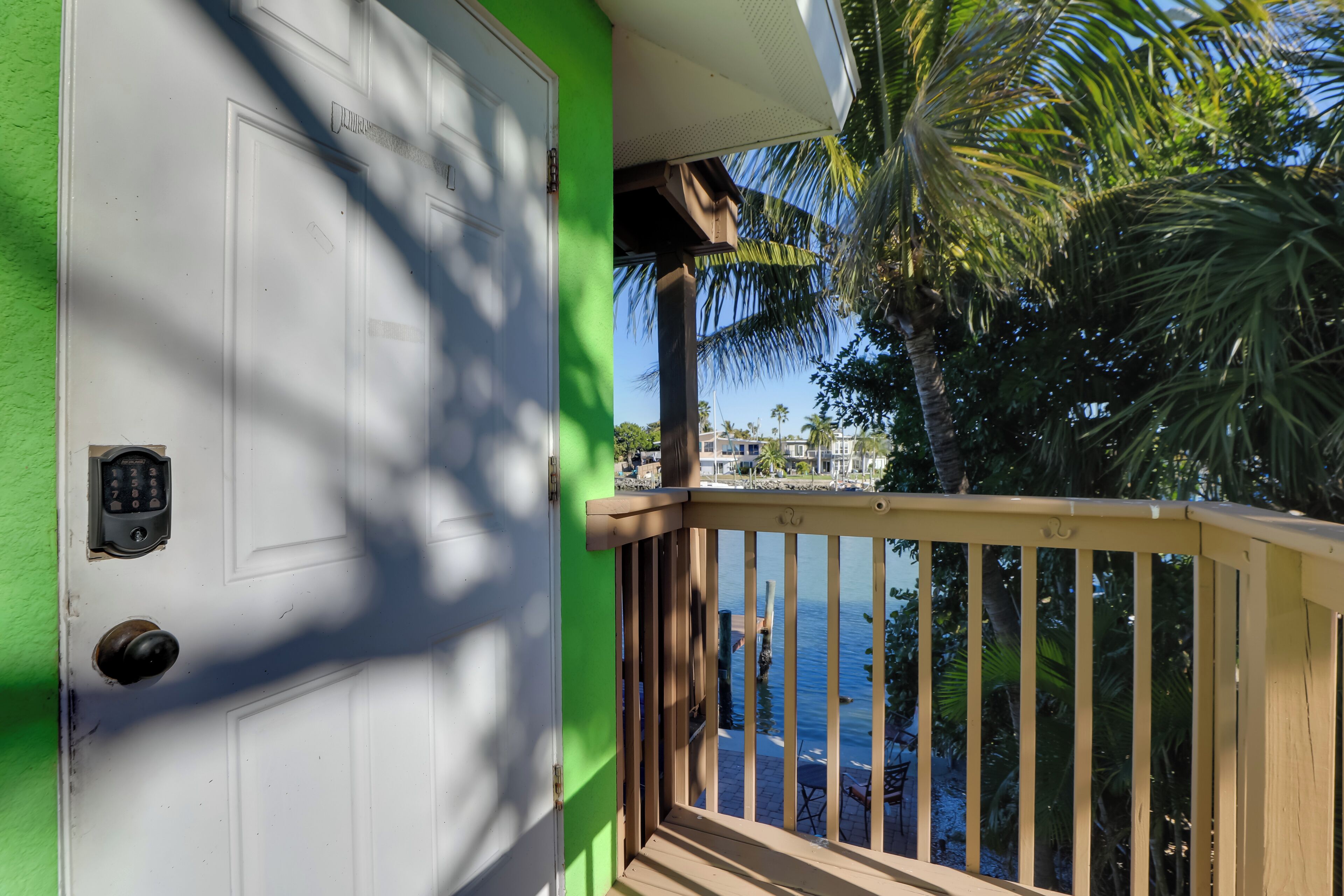 A white door with a keypad lock, a green wall, and a wooden balcony railing overlooking a body of water.