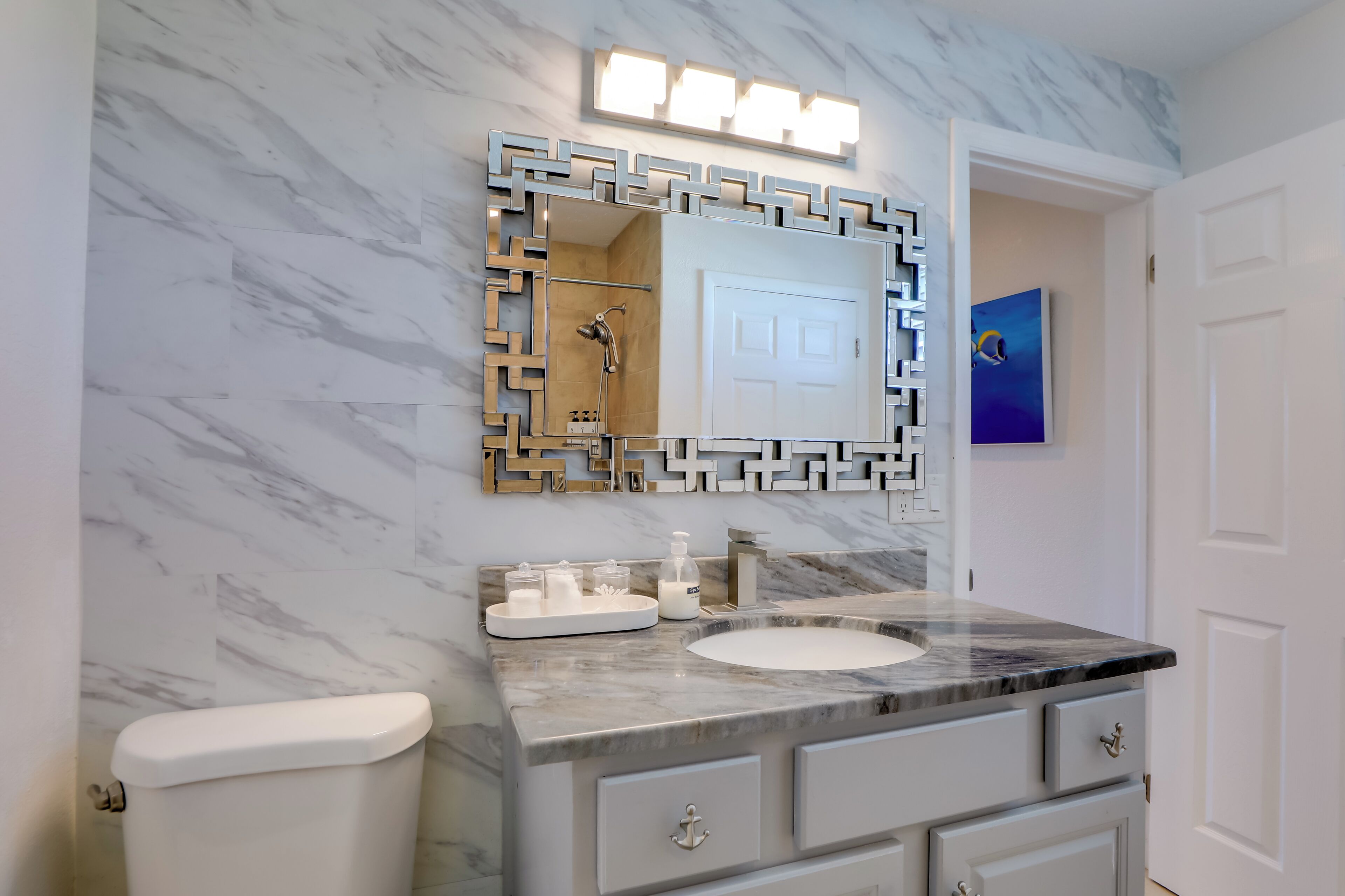 Une salle de bain avec un lavabo en marbre, des toilettes blanches et un miroir doté d’un cadre géométrique.