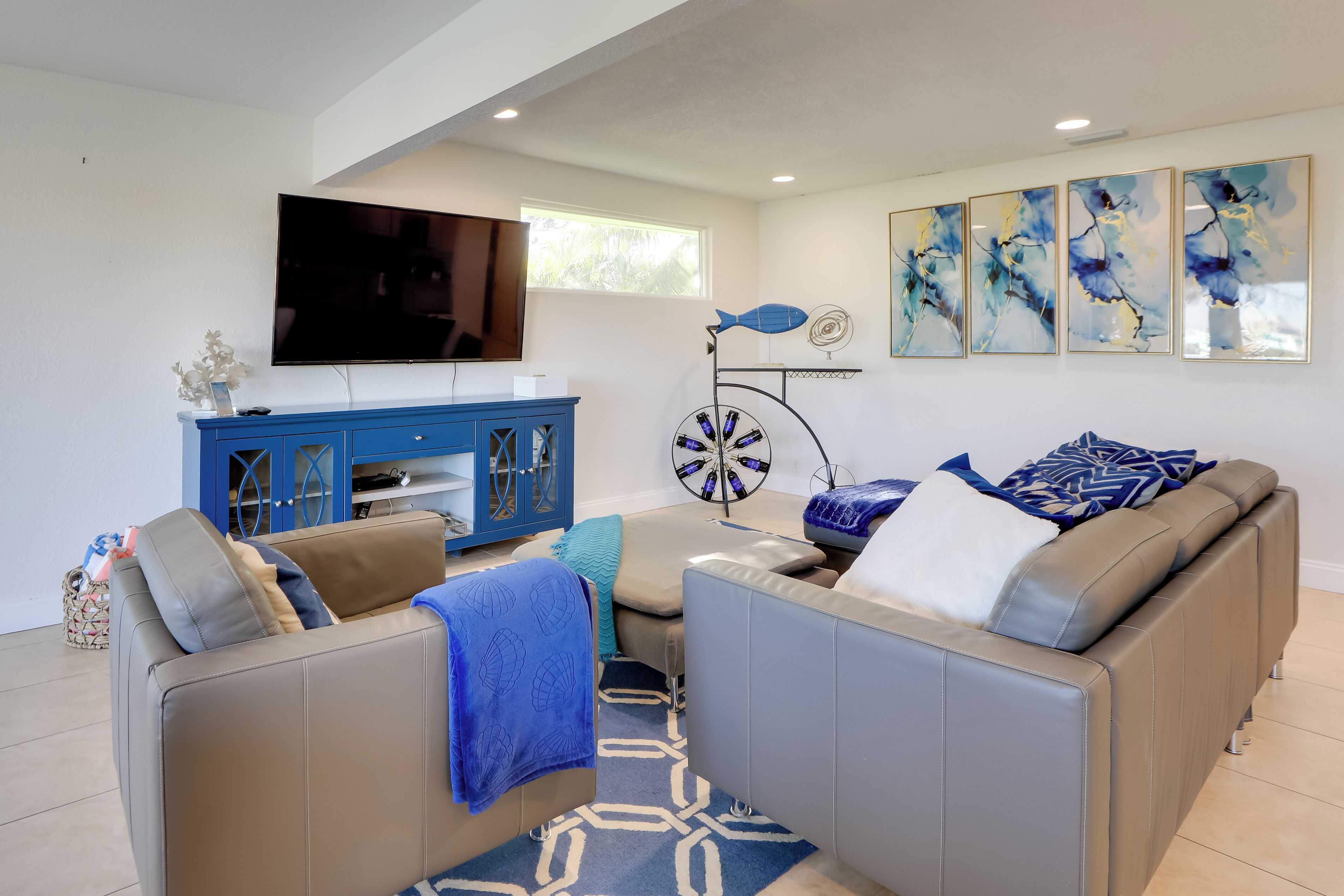 A modern living room with a large flat-screen TV, a blue cabinet, and abstract wall art.