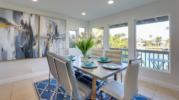 A dining area with a table set for four, white chairs, and a vase with white flowers. - 1 Block to Beach! Boutique Condo at Johns Pass (Madeira Beach)