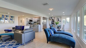 A spacious living area with a grey sofa and blue armchairs, a kitchen in the background, and large windows providing natural light. - 1 Block to Beach! Boutique Condo at Johns Pass (Madeira Beach)