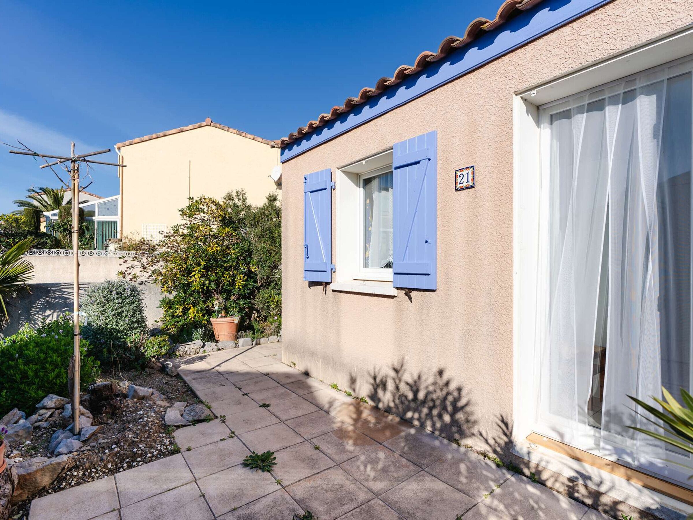 Ein Wohnhaus mit befestigter Auffahrt, einem kleinen Garten mit Blumentöpfen und einem blau verschlossenen Fenster.