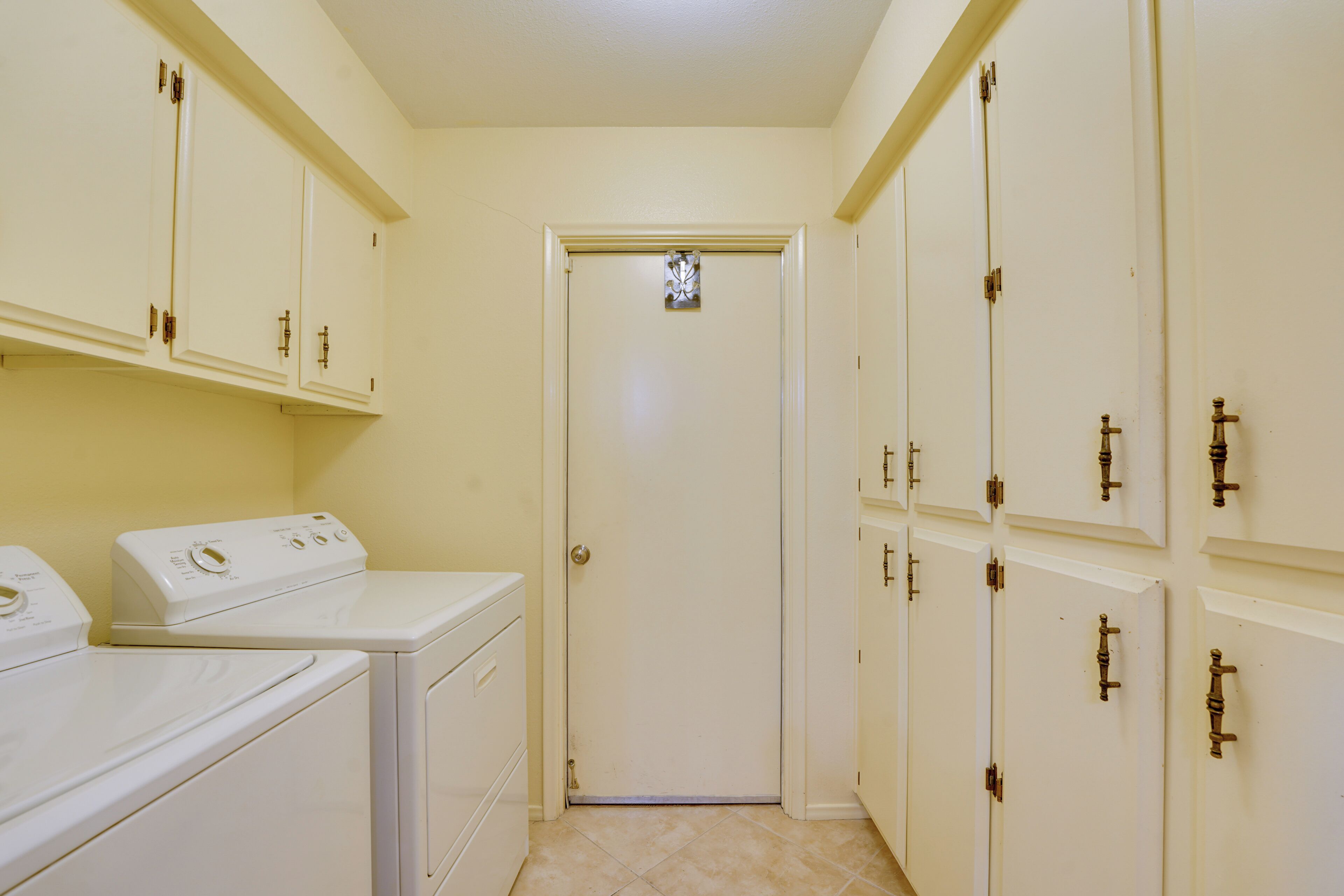 A laundry room with a washer and dryer, a door with a small window, and multiple cabinets with locks.