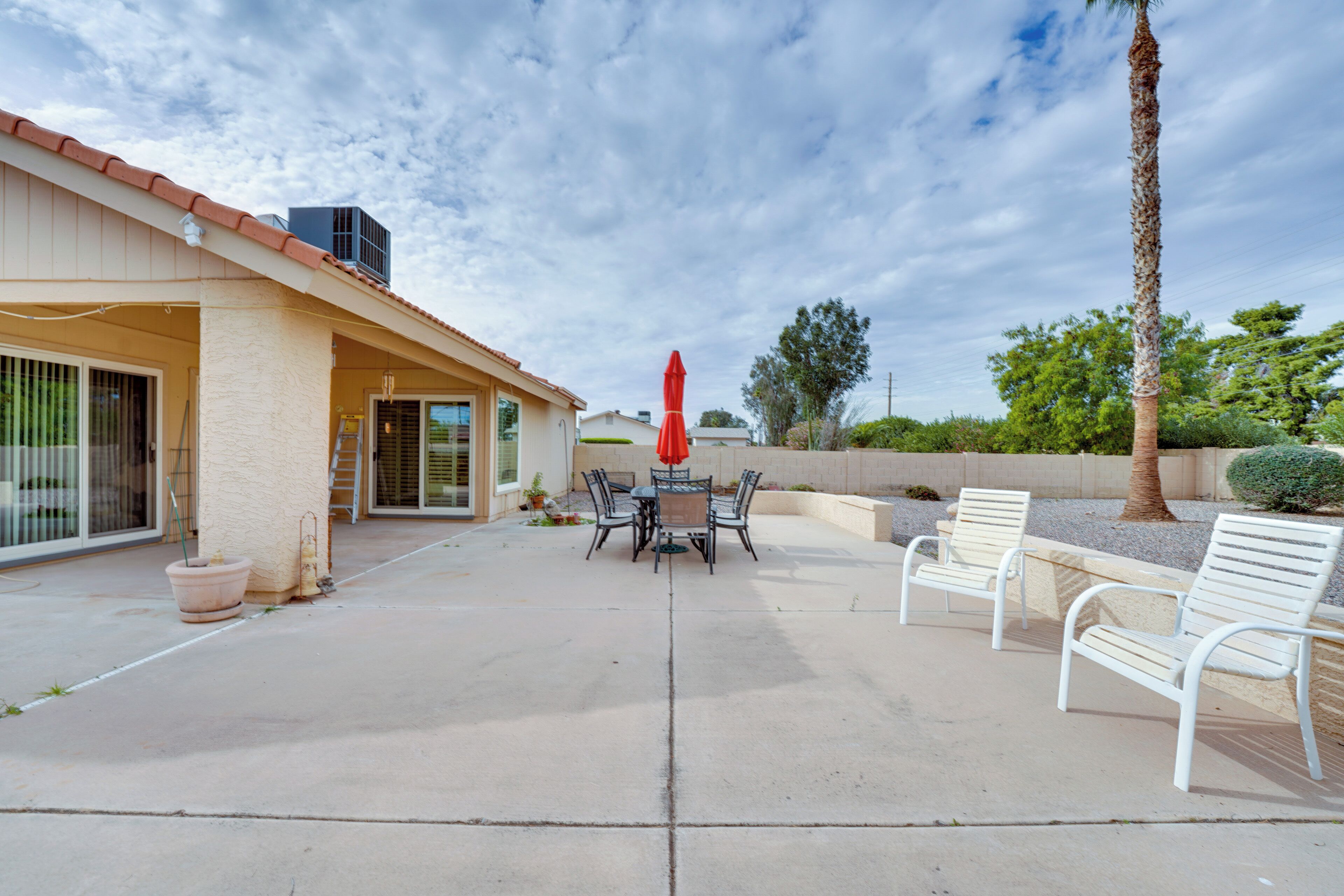 An outdoor patio with a table and chairs, a red umbrella, and a palm tree.