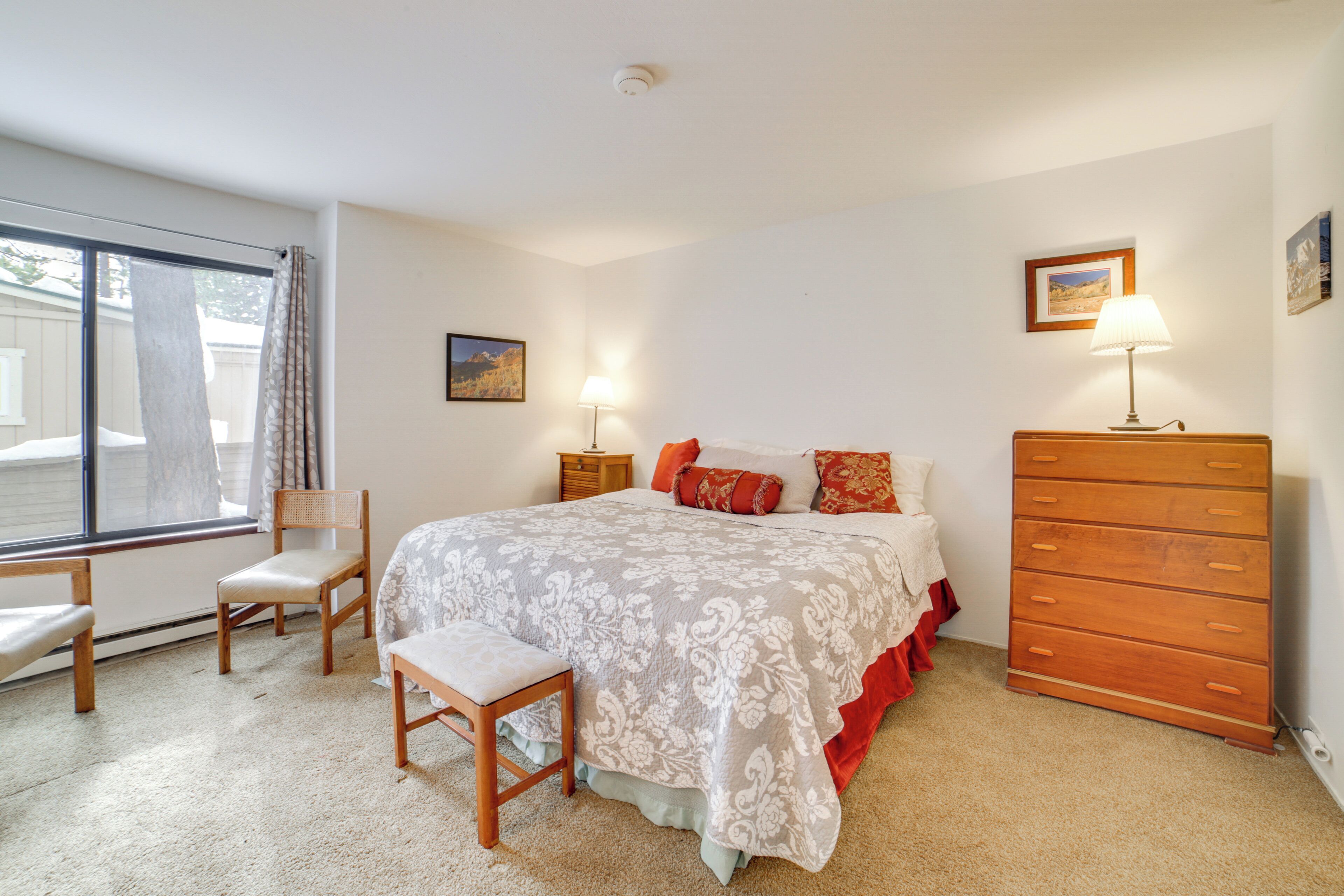 Une chambre à coucher avec un lit, une commode en bois, une chaise, un banc et une fenêtre avec des rideaux.