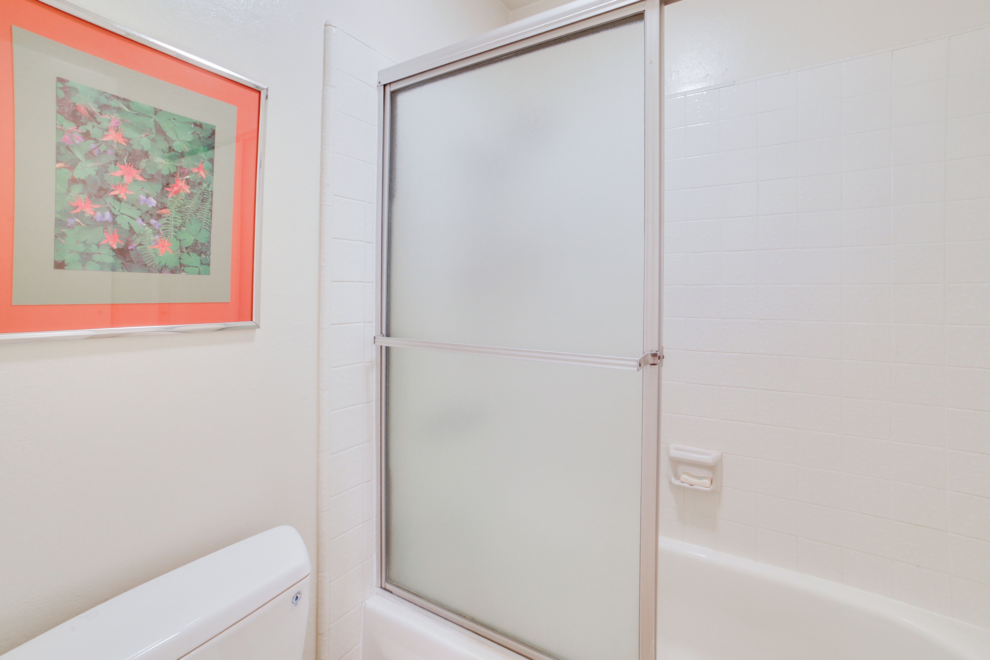 A bathroom with a glass shower enclosure, a toilet, and a framed artwork on the wall.